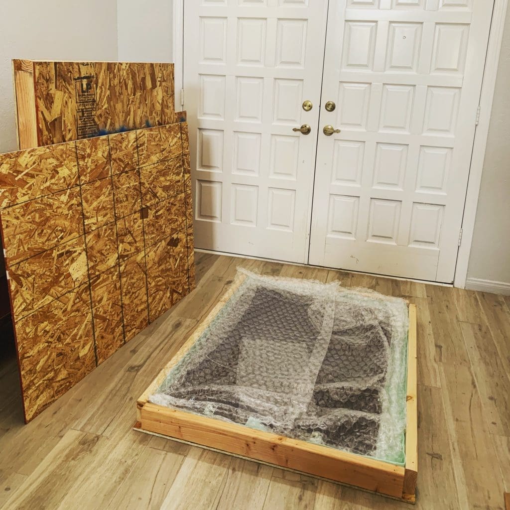 Custom wood crate with protective bubble wrap, stacked OSB boards in background, and double doors, illustrating craftsmanship in Las Vegas packaging solutions.