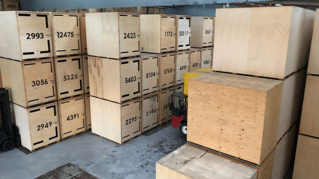 Wooden crates stacked in a warehouse, featuring various sizes and numbers, highlighting custom crate solutions for safe transport and storage.