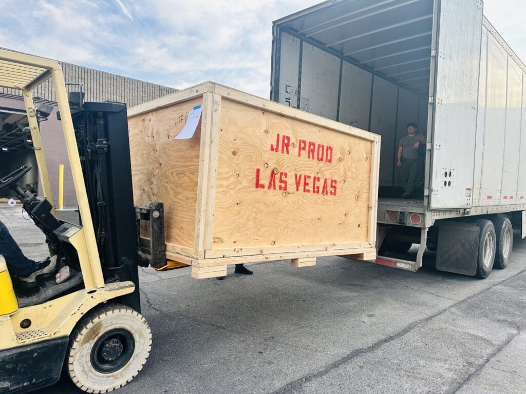 Forklift transporting custom wooden crate labeled "JR PROD LAS VEGAS" into truck for secure shipping of valuable items.